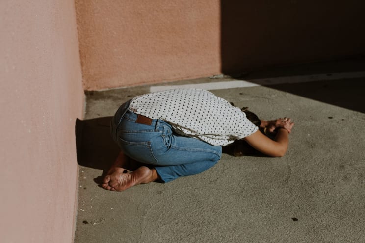 A Woman Leans Down With Her Head To The Ground Outside Against The Concrete