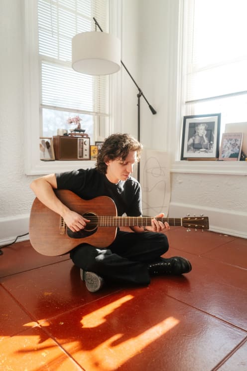 Young Man Sitting On The Floor Playing An Acoustic Guitar