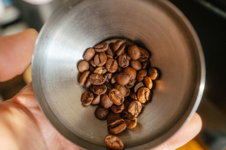 A Person Is Holding A Metal Bowl Of Roasted Coffee Beans