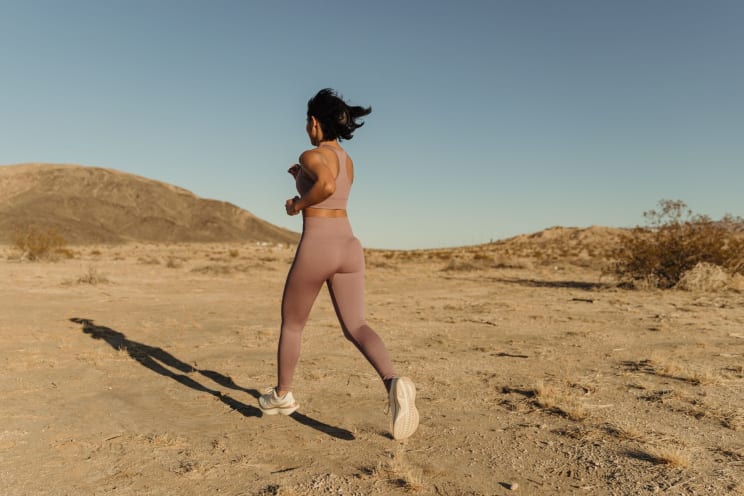 Woman Wearing Pink Sportswear Runs Across A Barren Terrain Under A Blue Sky