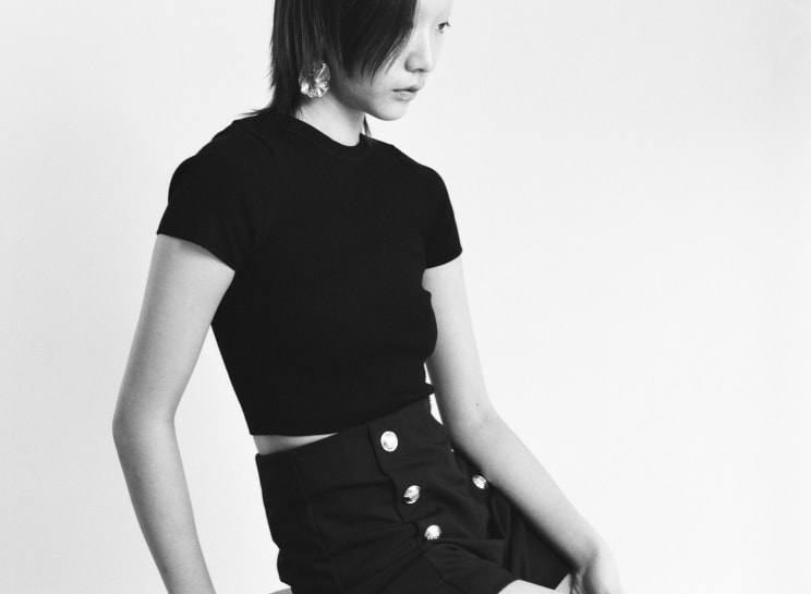 Portrait Of A Young Woman With Short Hair Wearing A Round Earring And Wearing A Black Shirt And Behind Her There Is A White Background