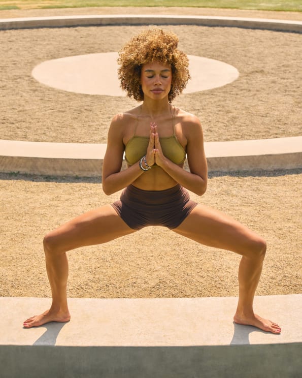 A Beautiful Woman In A Yoga Goddess Pose On A Garden Wall In The Bright Sunshine