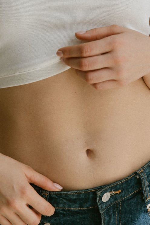 A Person In Jeans Lifts Their White Shirt To Reveal Their Midriff