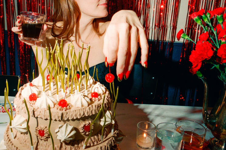 A Woman Holding A Cocktail And A Cherry Next To A Cake Covered In Candles