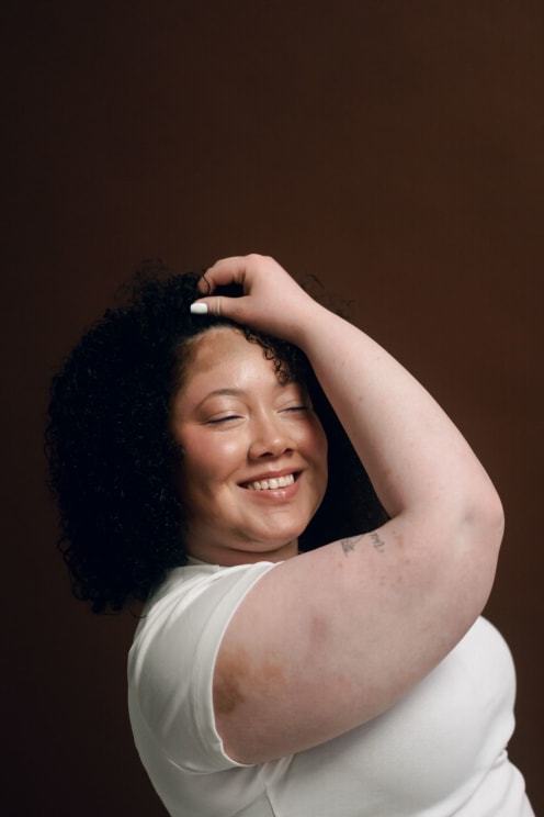 A Smiling Woman With Curly Hair Poses Confidently Against A Brown Background