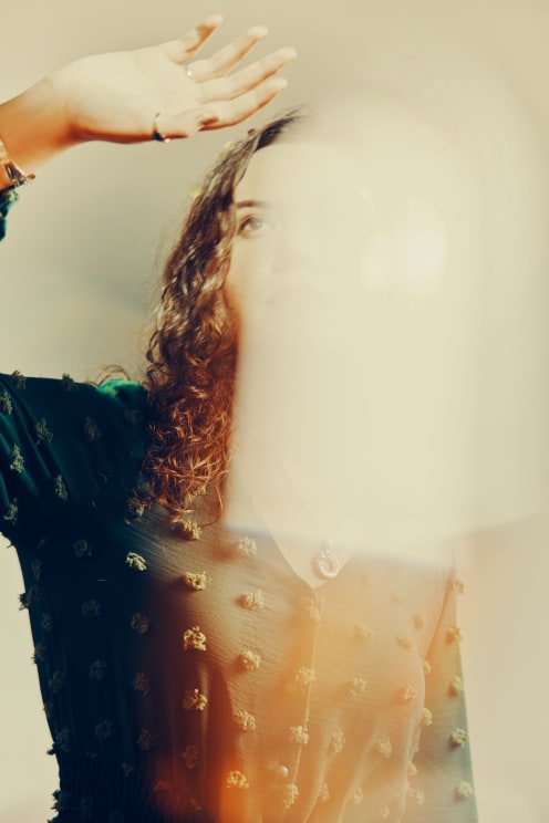 Dark Haired Woman Raising Her Hand With A Blur Of Light Covering Most Of Her Face