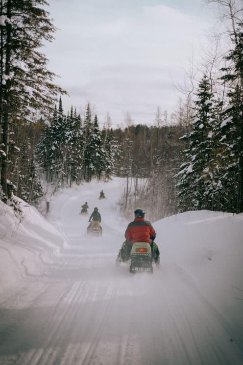 People Traveling On Snowmobiles Along A Snow Track In The North Woods Of Wisconsin