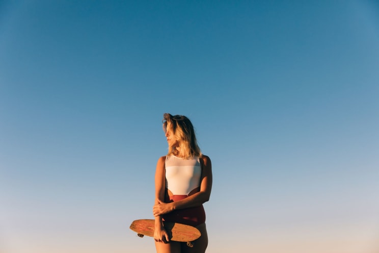 Blonde Woman In A Bathing Suit Holding A Small Skateboard
