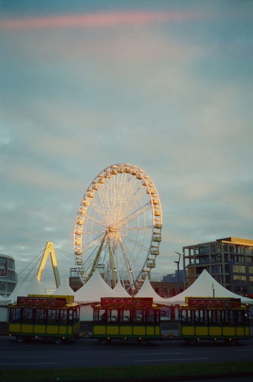 A Ferris Wheel In An Amusement Park With Train Cars Nearby