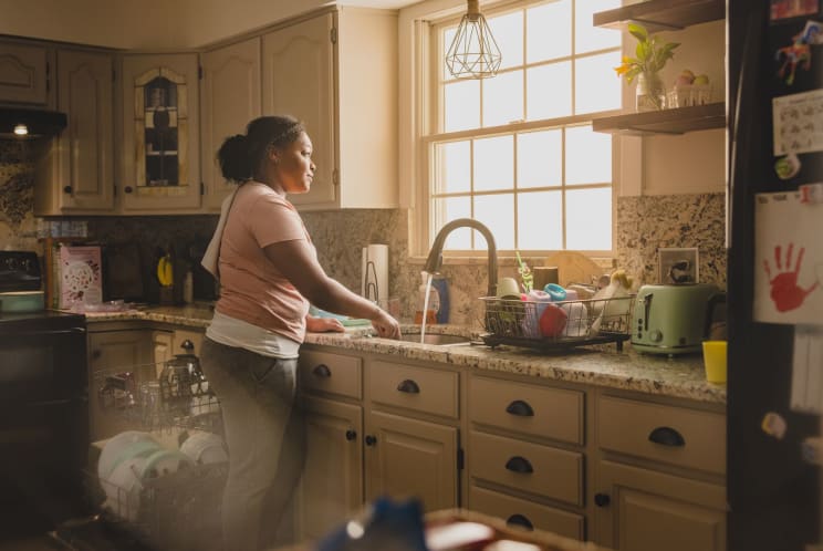Woman With Curly Hair Does Dishes And Loads Dishwasher In Kitchen