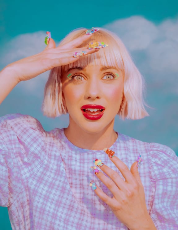 A Woman With Short Blonde Hair Holds Her Hand Over Her Eyebrow And Has Her Mouth Open