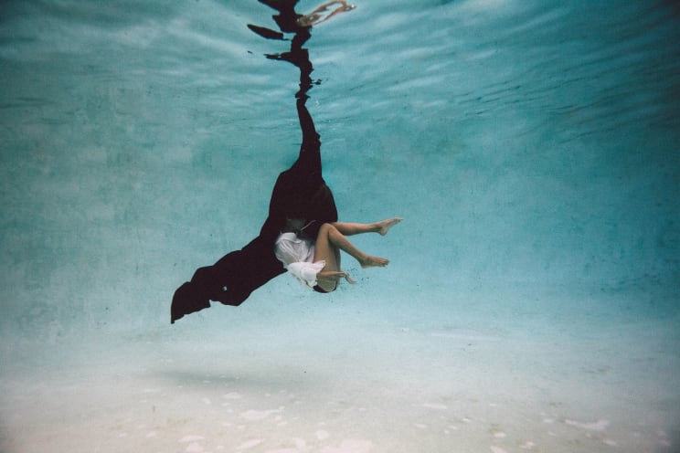A Woman Underwater With Her Legs Exposed And A Black Coat Covering Her Head