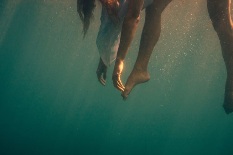 Woman Dressed In White Gesturing Underwater With Sun Reflections