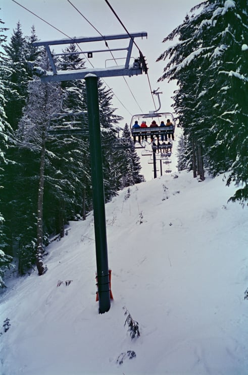 Five People Ride A Ski Lift Up A Snowy Mountain