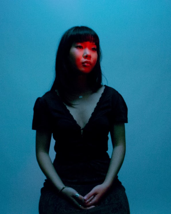 A Woman In A Black Dress Stands Looking Into The Distance With A Red Light Shining On Her Face