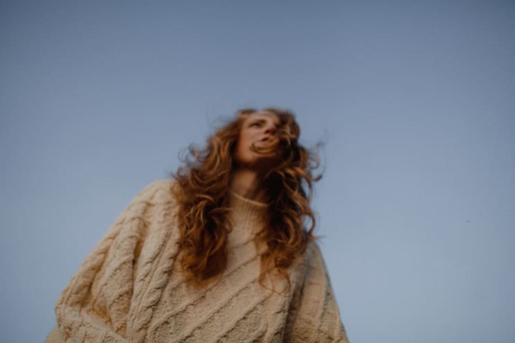 A Woman Standing Outdoors Wearing A Sweater During Dusk With A Blue Sky In The Background