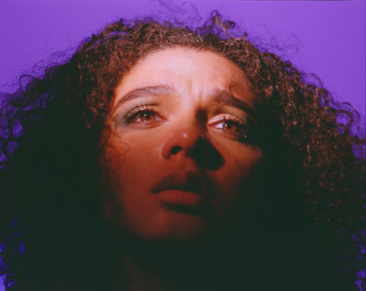 Close Up Of A Young Woman With Curly Hair Against A Violet Background