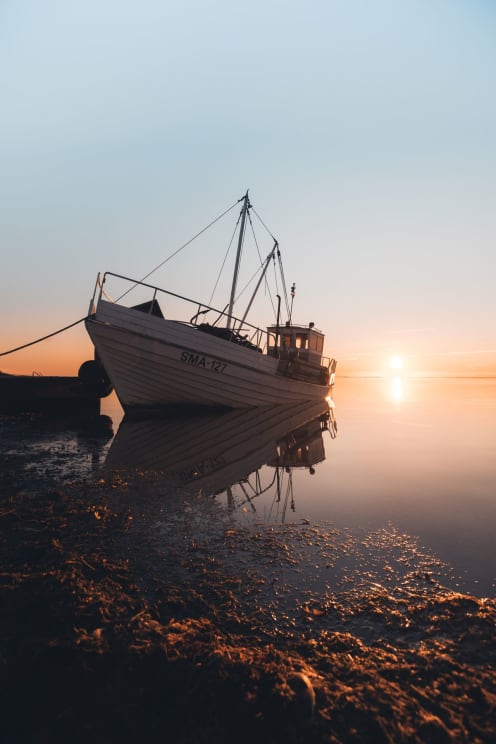 A Fishing Boat Docked On The Shore During Sunset