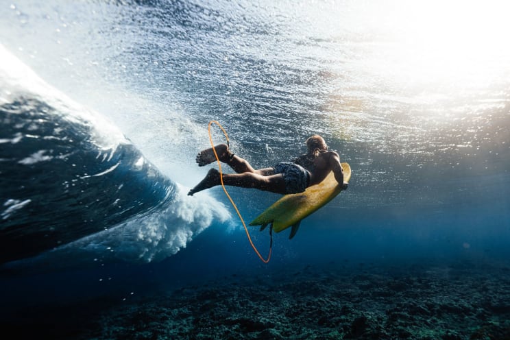 A Girl Swims Underwater Near A Big Wave While Holding Onto Her Paddleboard