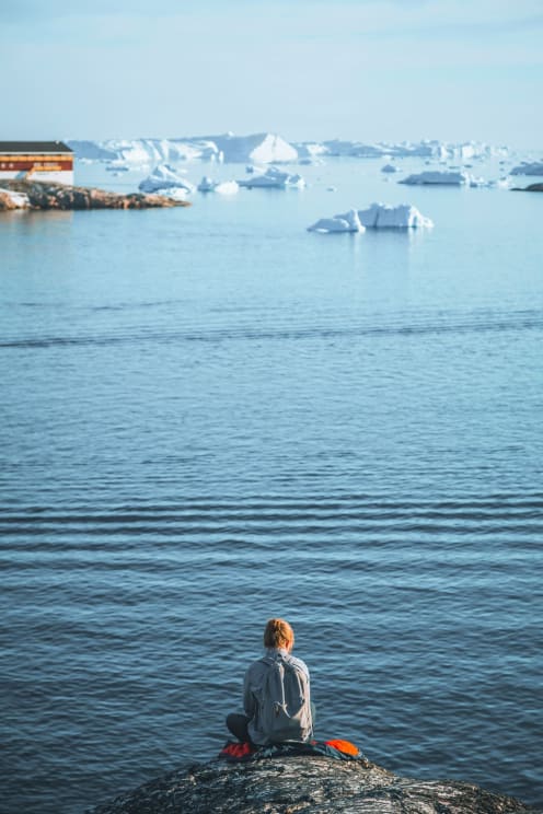 A Woman Sits On A Rock Observing The Sea With Icebergs