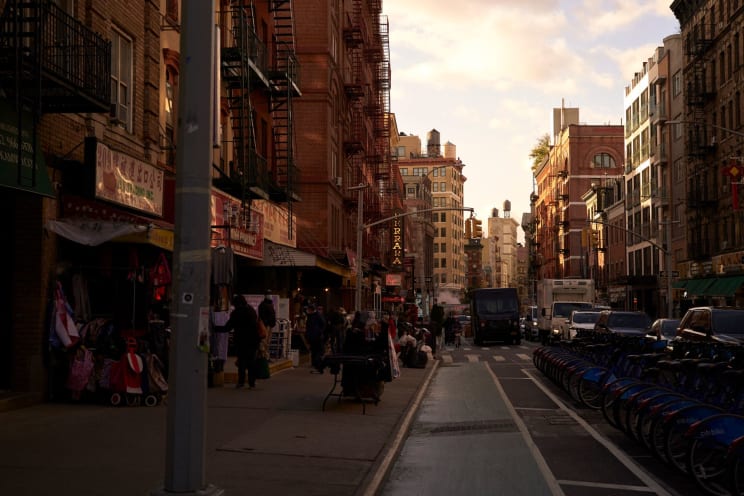 A Bustling City Street With Buildings Cars And A Crowd