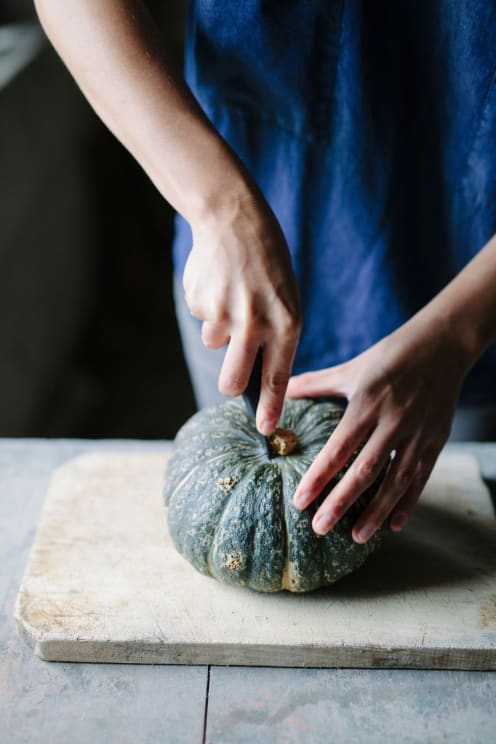Woman Cutting A Small Green Pumpkin On A Cutting Board In The Kitchen