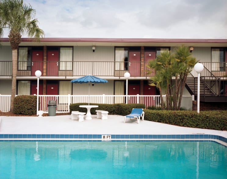 Umbrella Covered Furniture Stands Between Motel And Swimming Pool