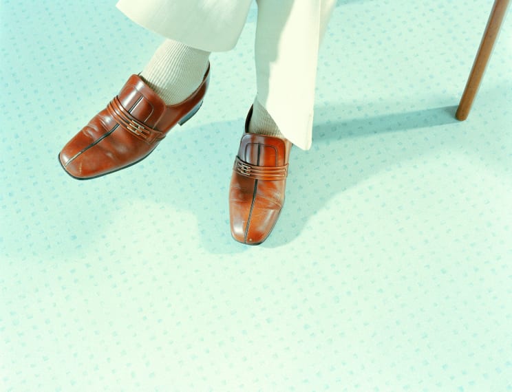 A Person Wearing Penny Loafers Is Seated Revealing A Green Dotted Floor