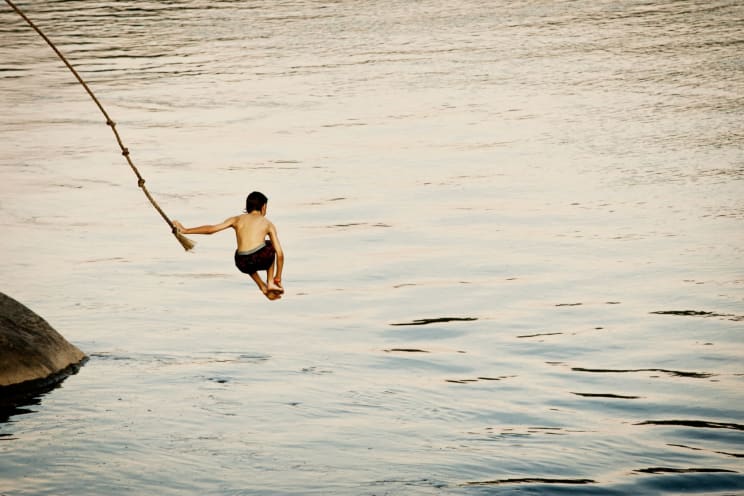A Boy Jumps Off A Rope Swing Into A Lake