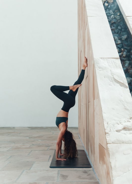 A Young Woman Is Practicing Yoga By Doing A Handstand On A Yoga Mat Indoors