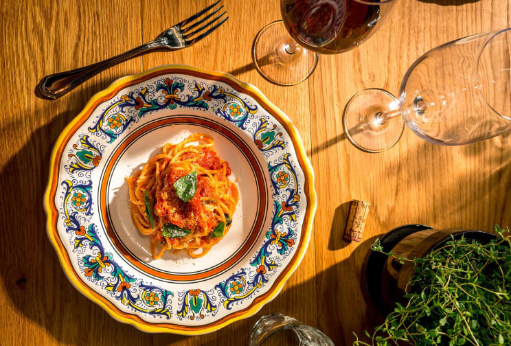 A Pasta Dish Is Placed Beside Wine Glasses And Potted Herbs