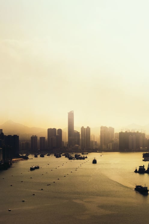 A Cityscape And Water At Sunset Silhouetted Against A Yellow Sky With Boats In The Water