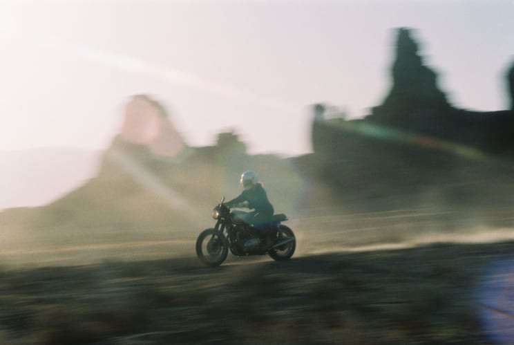 A Person Wearing A Helmet Coat And Pants Rides A Motorcycle In The Desert