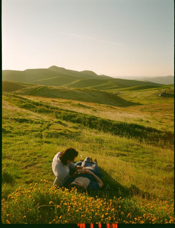 A Couple Lying On A Grassy Hill On A Sunny Day In Nature