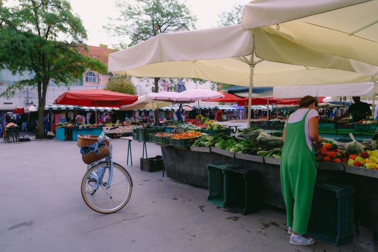 A Woman In A Green Jumpsuit Shops At A Farmers Market