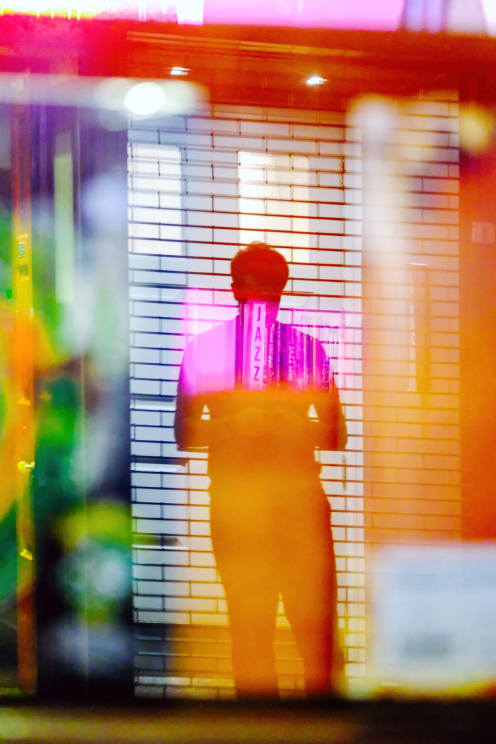 Neon Sign And Other Colored Lights Cover Silhouette Of Man Walking Through Doorway