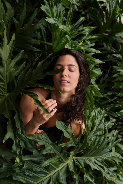 A Smiling Woman With Her Eyes Closed Between Plant Leaves