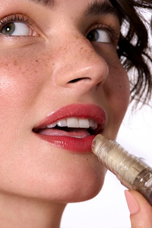 A Portrait Of A Young Woman Applying Lipstick To Her Lips