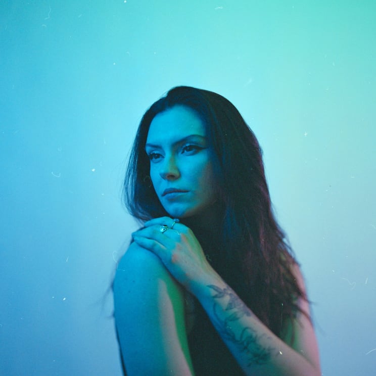 A Woman With Long Hair And Tattoos, Bathed In Blue Light, Poses For A Picture