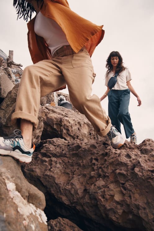 Two Women Are Hiking Along A Rocky Coastal Region On An Overcast Day