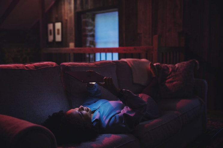 A Black Woman Lies On The Couch In Her Living Room While Holding A Tablet