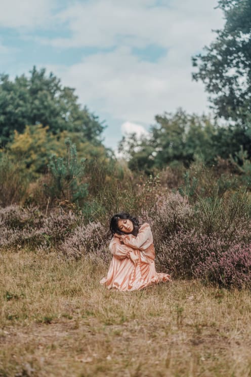 Woman Sitting In A Lush Environment Wearing A Long Pink Satin Dress