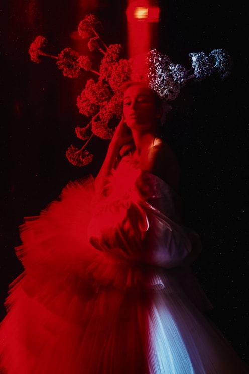 A Lady Poses With Her Head Lean Closely To Flowers Behind Her In A Neon Lighted Room