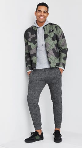 Men’s athleisure clothing including a grey mens hoodie, camo jacket, grey joggers and black sneakers.