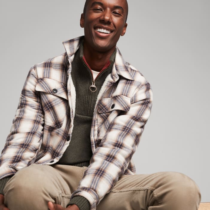 Model wearing Stitch Fix men’s clothing including a flannel shacket, a quarter zip sweater and tan pants.