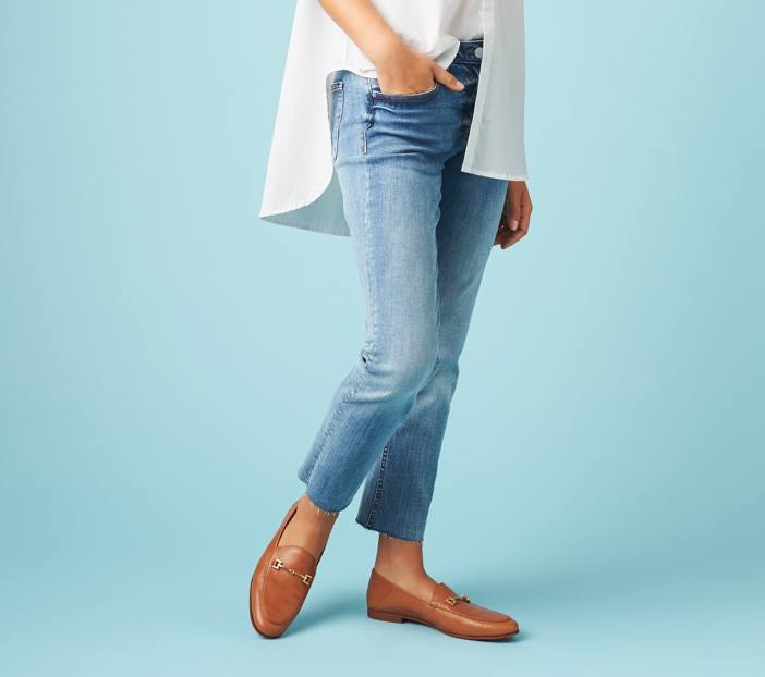 White high-low shirt with raw hem ankle length jeans and brown loafer shoes.