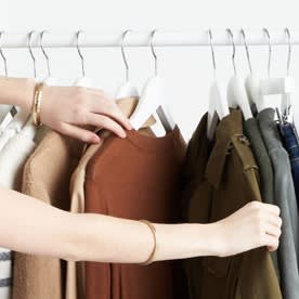 Hands reaching toward a rack with shirts.