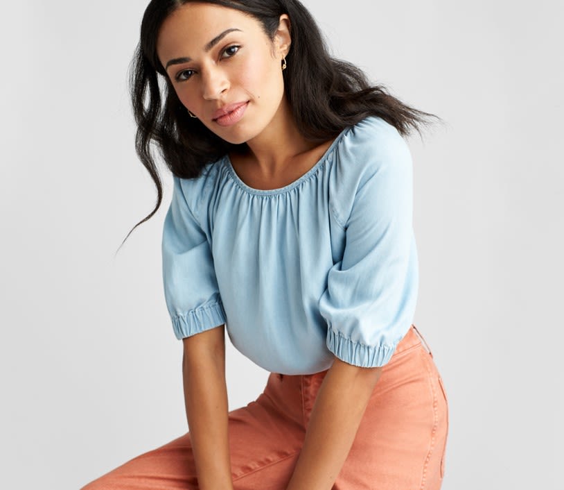 Woman wearing Stitch Fix clothing including light blue top and light orange jeans