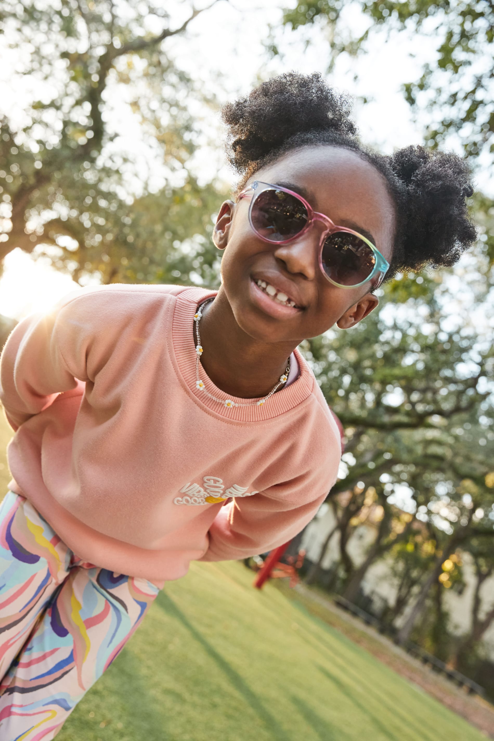 Kids: Girl in park wearing Stitch Fix pink sweatshirt and colorful leggings with sunglasses