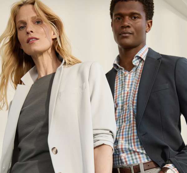 A woman in a Stitch Fix light gray blazer and a man in a Stitch Fix dark blazer with a checked shirt pose confidently, looking at the camera in a well-lit space.